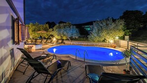 Une piscine avec des chaises longues et un mur en pierre, entourée d’arbres et d’un bâtiment.