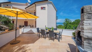 Une terrasse avec des meubles d’extérieur, un parasol jaune et une cheminée en pierre.