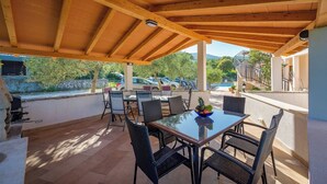 An outdoor patio with a wooden ceiling, a glass table, and black wicker chairs. - Relaxing Summer Apartment - Pool, Sauna, Jacuzzi 6 (Drenje)