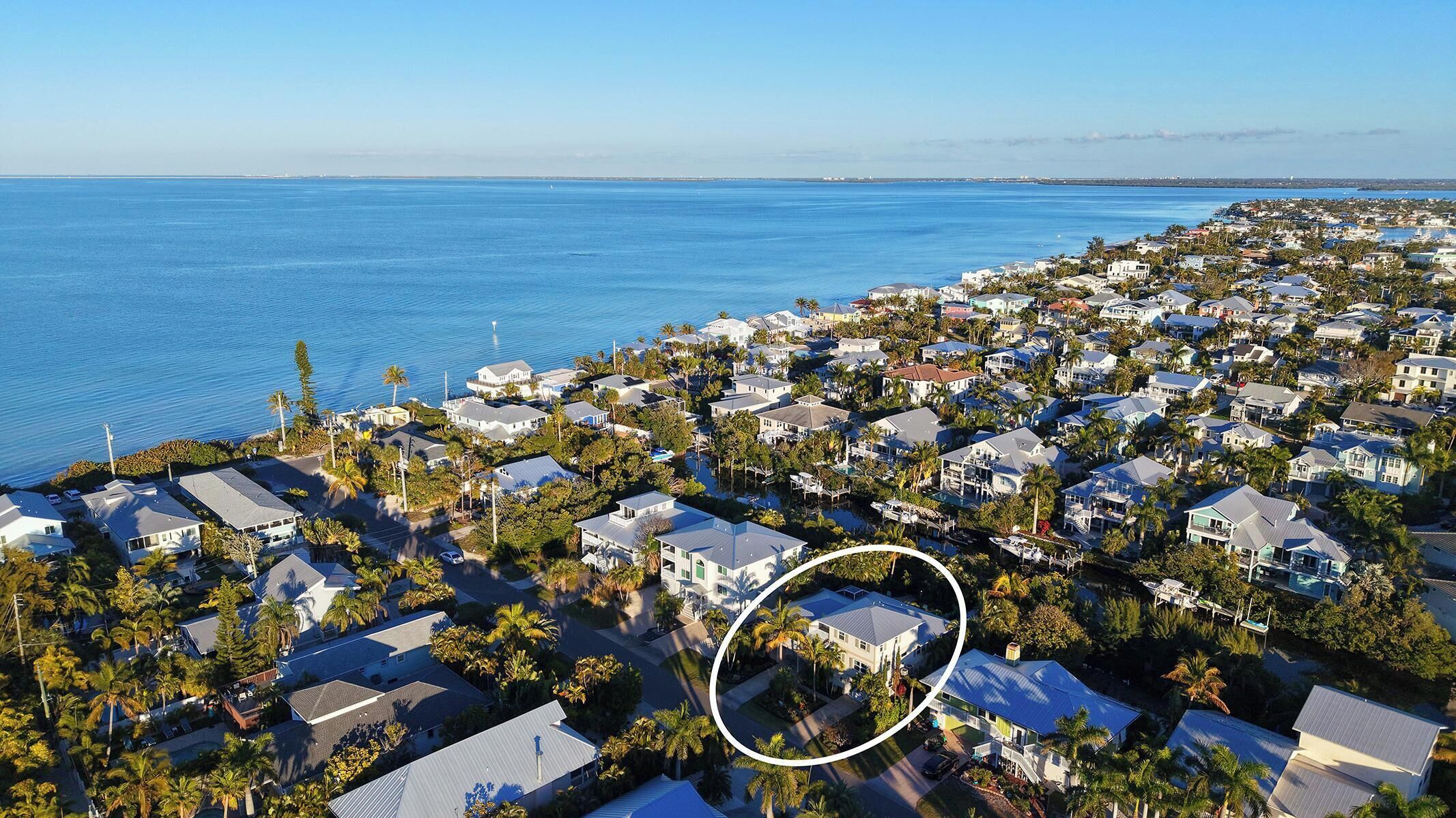 Luchtbeeld van een kustgebied met woningen, palmbomen en een helder uitzicht op de oceaan.