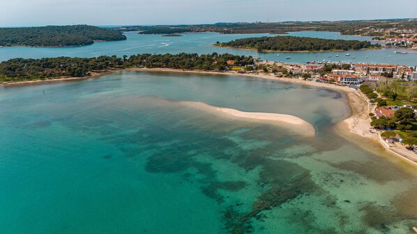 An aerial view of a coastal area with clear waters, a sandy beach, and a town with buildings along the shore. - Pool Apartment Sax with Sea View (Private Pool) (Medulin)