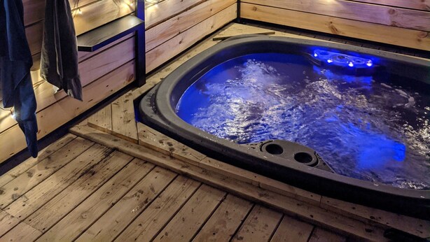 Une terrasse en bois avec un jacuzzi, des guirlandes lumineuses et une serviette accrochée au mur.