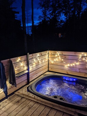 A wooden deck with a hot tub, string lights, and a towel hanging on the wall.