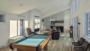 Un grand espace de vie comprenant une table de billard, des sièges confortables et un coin cuisine.