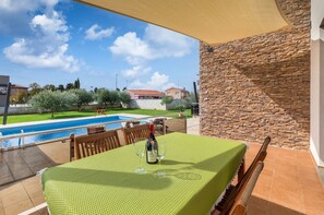 En terrasse med et bord dækket til to, med udsigt til en pool og en stenvæg.