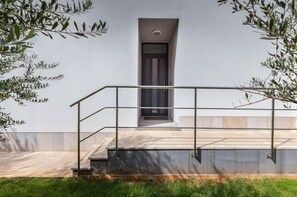 Stylish entrance with a metal staircase and glass railing, set amidst a serene landscape with olive trees.