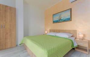 A bedroom with a bed, a nightstand, a wooden wardrobe, and a painting of a ship on the wall.
