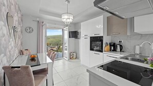 A modern kitchen with white cabinets, a black stove, and a large window. - Lady M Gold - Balcony and Sea View (Rabac)