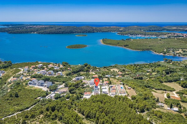 An aerial view of a coastal town with a marina, residential buildings, and surrounding greenery.