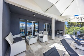 An outdoor seating area with wicker furniture, glass doors, and umbrellas.