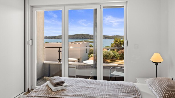 A bedroom with a large sliding glass door leading to a balcony with a view of a lake and buildings. - Villa Pura Vida - Private Pool, Sea View (Pomer)