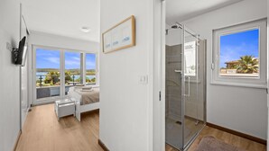 A modern bedroom with a large window, a bed, a TV, and a glass shower. - Villa Pura Vida - Private Pool, Sea View (Pomer)