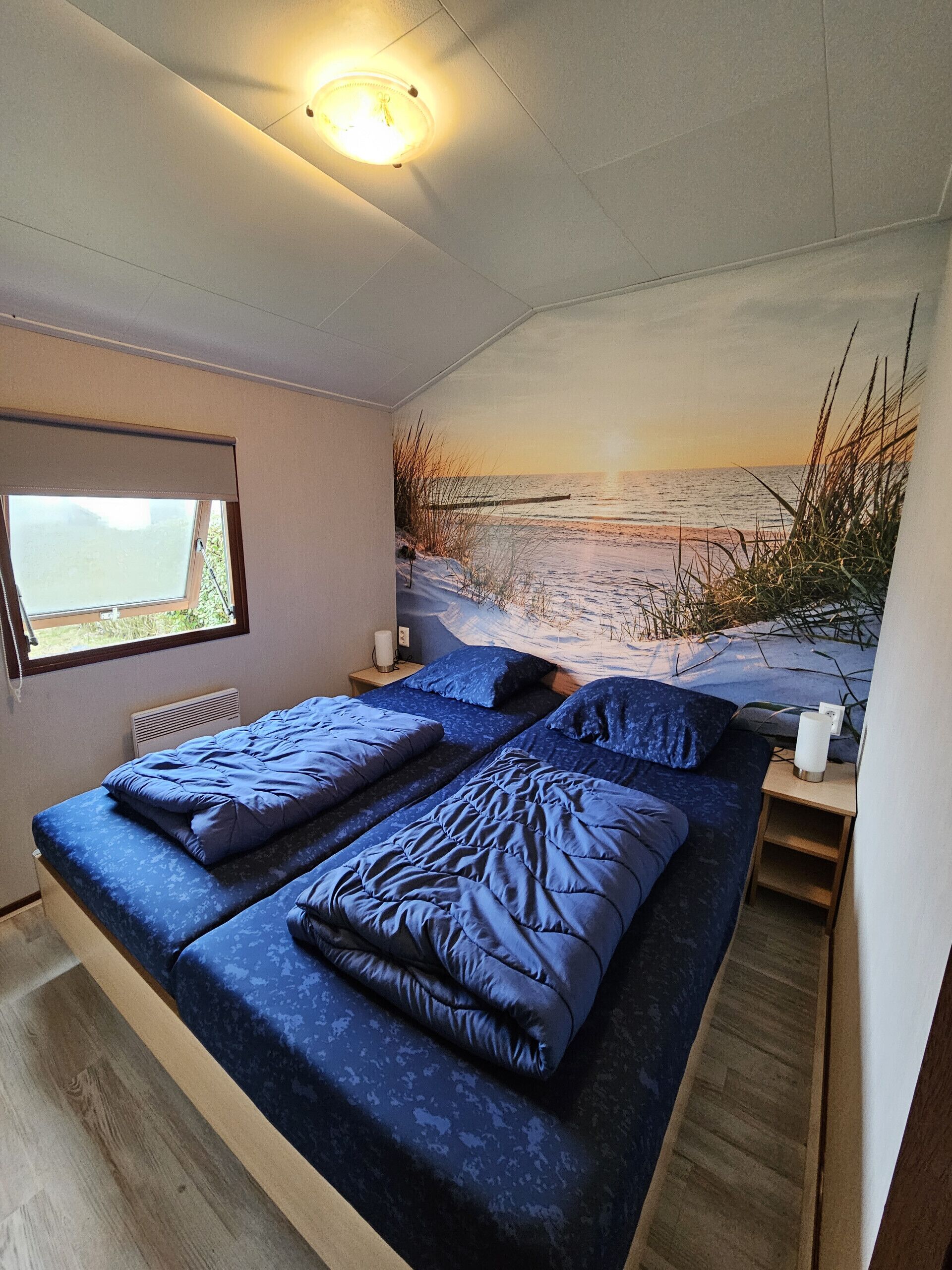 Une chambre avec deux lits, une fenêtre et une fresque murale représentant une plage.
