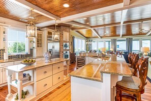 Une cuisine spacieuse dotée d’un grand îlot central, d’un plafond en bois et d’appareils électroménagers modernes.