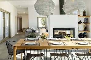 A dining area with a wooden table set for four, surrounded by black chairs. A fireplace is visible in the background, and there are hanging light fixtures above the table. - Villa Elia, superb 5-bedroom house with sea views (Chrisi Akti)