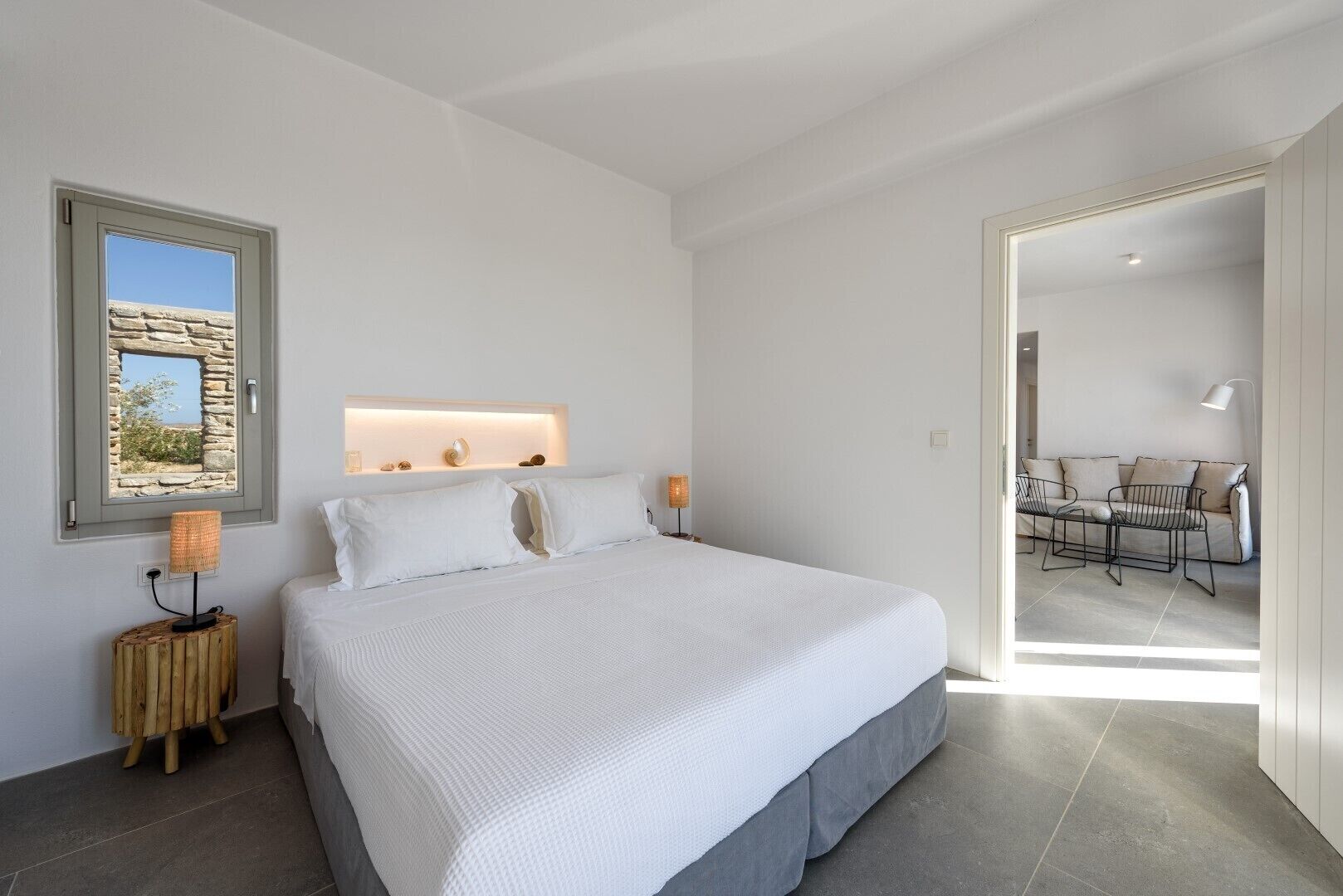 A modern bedroom with a large bed, a stone wall feature, and a view of an outdoor seating area.