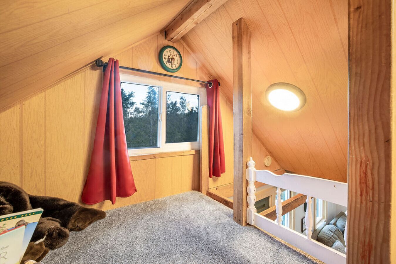 Un dormitorio acogedor en el ático, con techo inclinado, una cama nido de madera, ventana con cortinas y un reloj de pared.