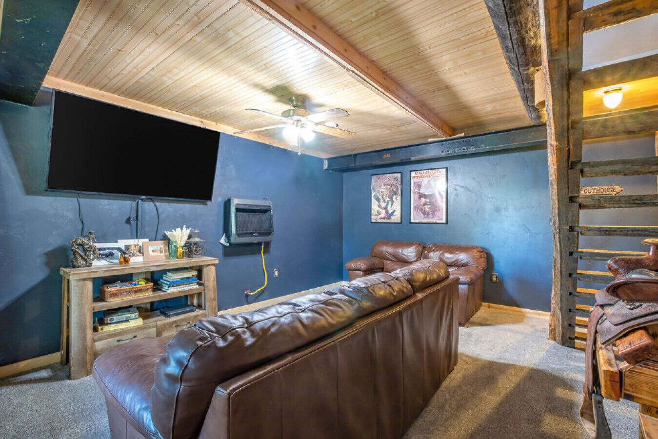Een gezellige kamer met een plafondventilator, een ingebouwde televisie, een leren bank en een houten ladder.