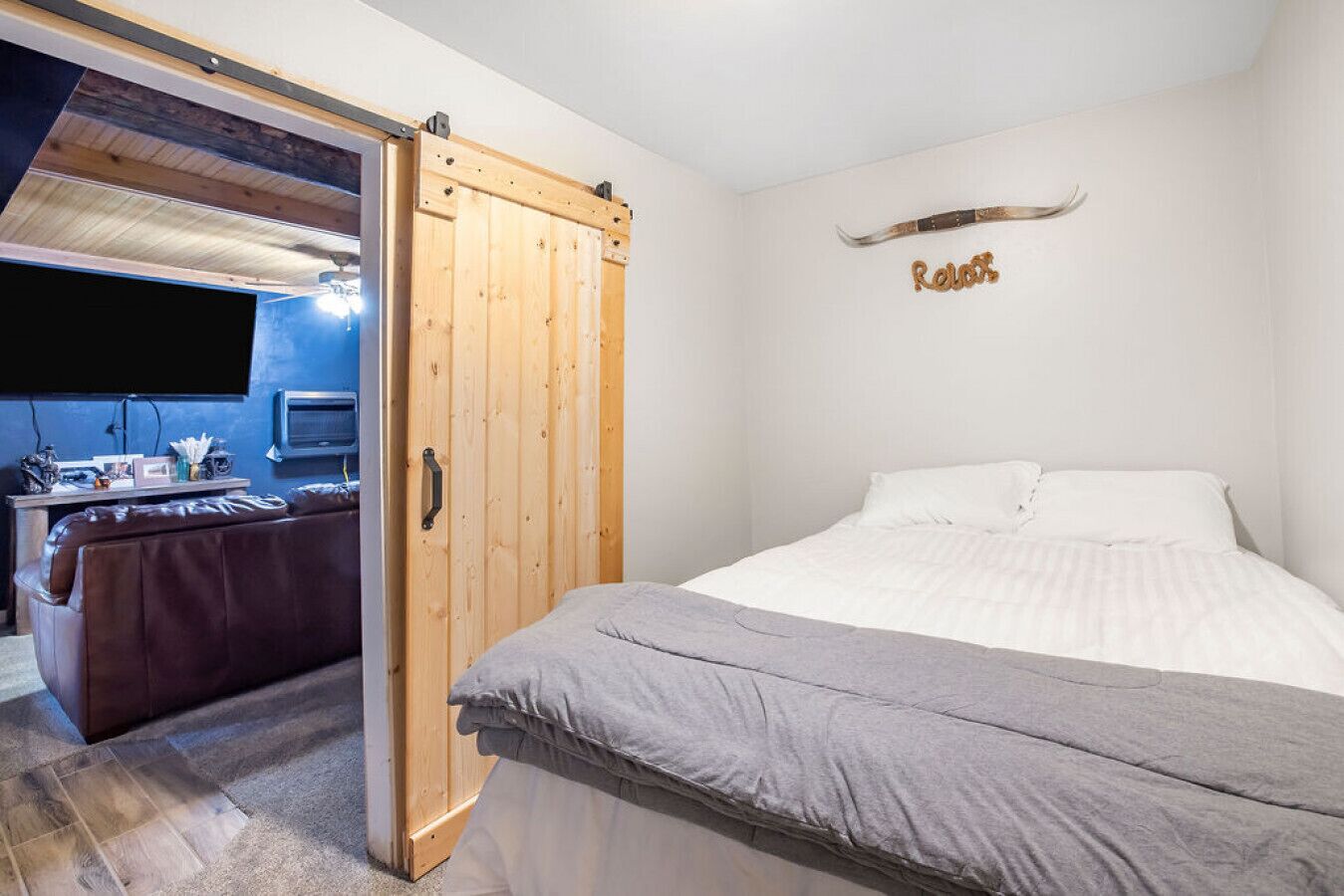 A bedroom with a bed, a wooden wardrobe, a desk with a computer, and a TV.