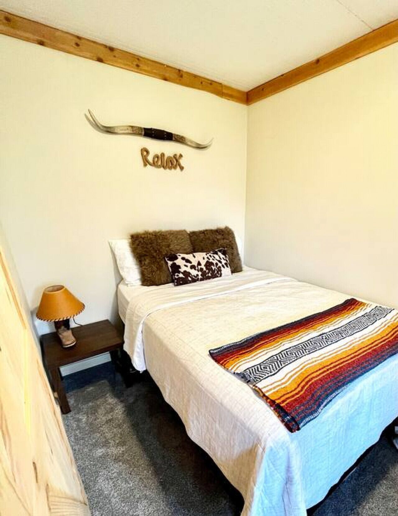 A bedroom with a bed, a nightstand with a lamp, a wooden headboard, and a wall-mounted decoration.