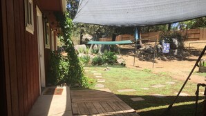 A wooden deck with a concrete pathway leading to a house. There is a garden with various plants and a fenced area with rocks and a hammock. - Sleeping Wolf Guest House (Oakhurst)