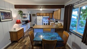 A compact kitchen with wooden cabinets, a dining table with chairs, a refrigerator, and a stove. - Sleeping Wolf Guest House (Oakhurst)