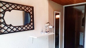 Un couloir avec un mur blanc, un miroir décoratif et une petite étagère sur laquelle se trouvent une lampe et une figurine.