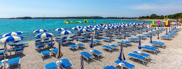 A beach with rows of blue and white striped umbrellas and sun loungers. - Istriensonne 0041 - Lucano-1 with sea view, large garden and parking lot (Medulin)