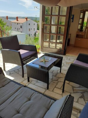 A balcony with wicker furniture, a table, and a view of buildings in the background. - Istriensonne 0041 - Lucano-1 with sea view, large garden and parking lot (Medulin)