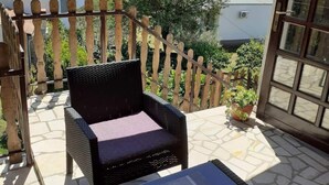 Un balcon avec une chaise en osier et une petite table, donnant sur un quartier résidentiel avec des maisons et des arbres.