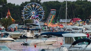 Un port de plaisance avec des bateaux amarrés, une grande roue et une attraction colorée en arrière-plan.