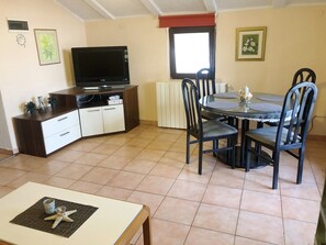 A dining area with a round table and chairs, a television on a cabinet, and a window with blinds. - Istriensonne 0041 - Lucano-1 with sea view, large garden and parking lot (Medulin)