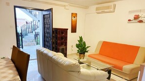 A living room with a white sofa, orange couch, and a glass coffee table. There is a plant on the table and a wooden cabinet in the background. - Istriensonne 0043 - Lucano-3 with a  large garden, two balconys, 2 air conditions and parking lot (Medulin)