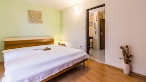 A bedroom with a wooden bed, a bedside table with a lamp, a vase with dried flowers, and a door leading to another room. - Istriensonne 0043 - Lucano-3 with a  large garden, two balconys, 2 air conditions and parking lot (Medulin)