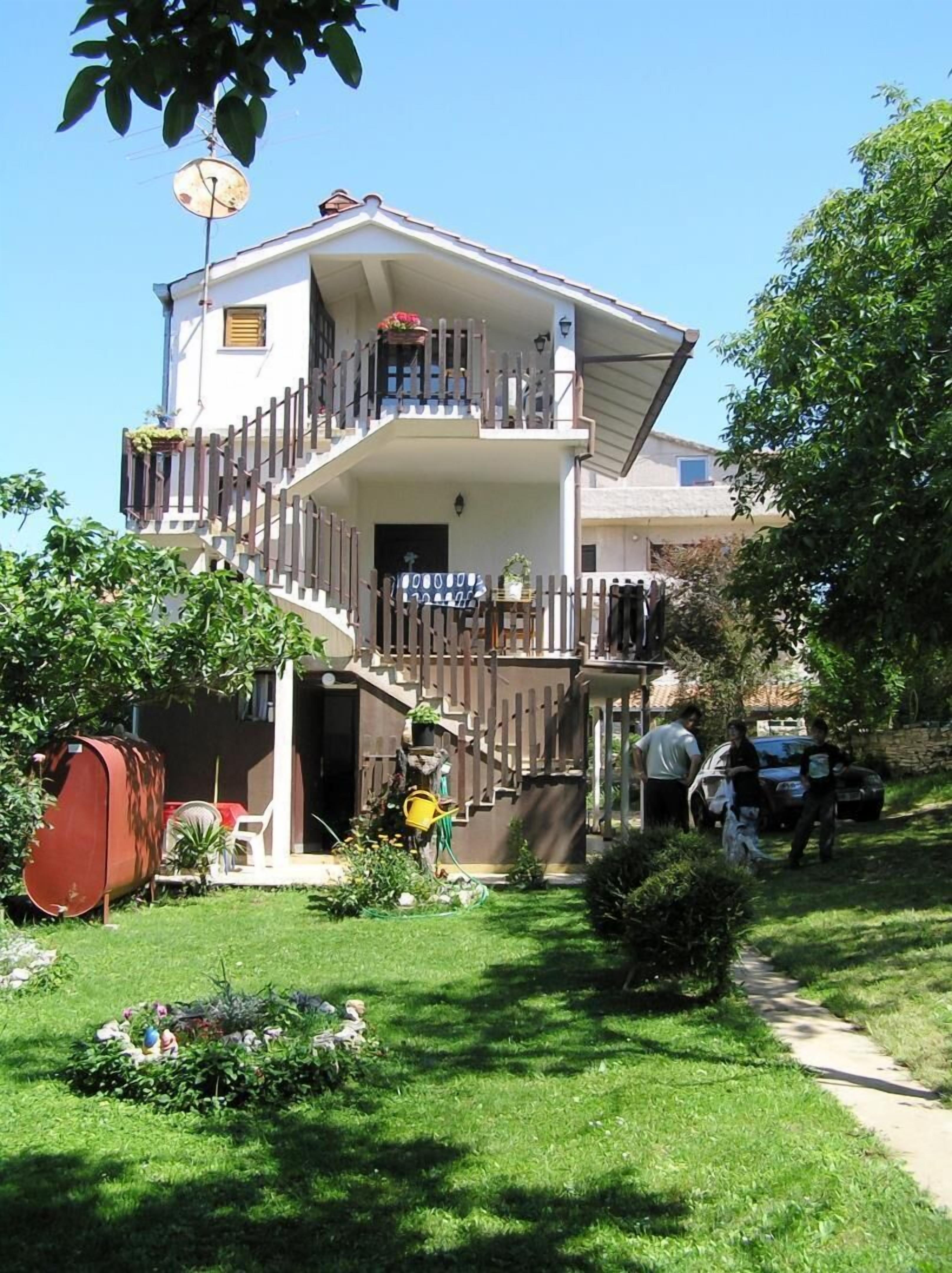Ein zweistöckiges Gebäude mit Balkon, Garten und einem Weg zum Eingang.