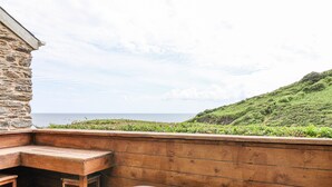 Une terrasse en bois dotée d’un jacuzzi et d’un espace salon, offrant une vue sur le paysage côtier.