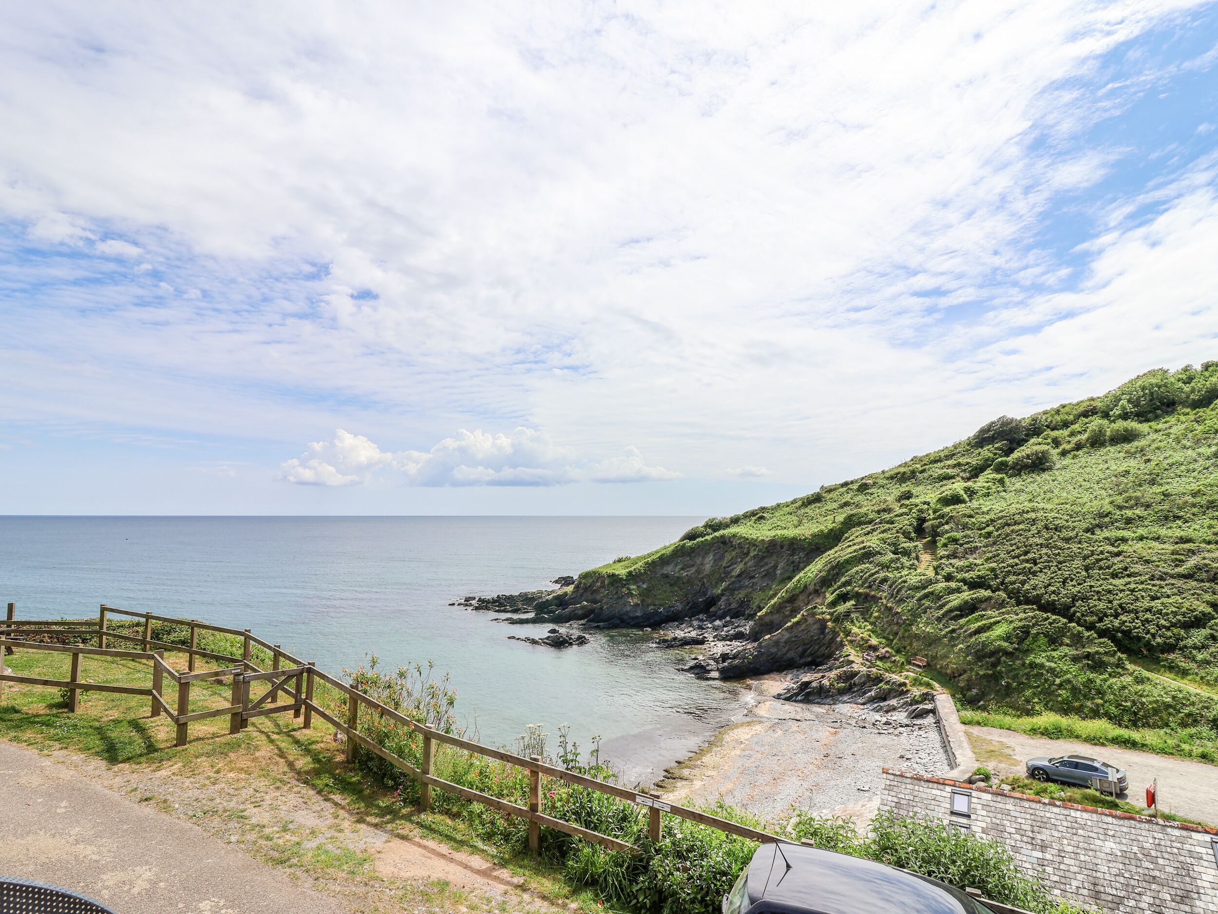 A coastal area with a wooden fence, a paved path, and a car parked on the side.