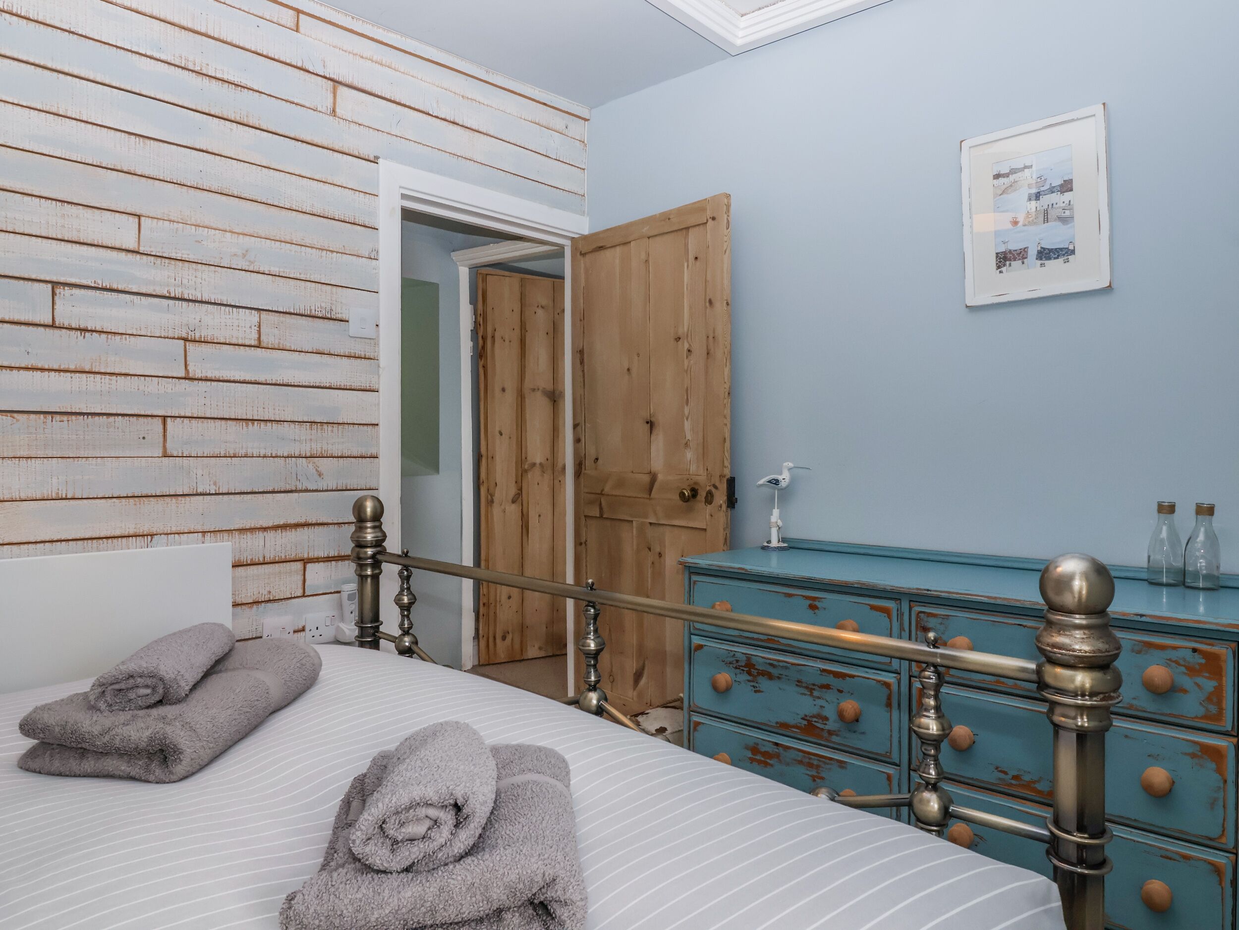 A bedroom with a bed, a wooden door, a dresser, and a framed picture on the wall.