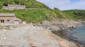 Un bâtiment en pierre situé sur la côte, avec une façade en pierre et une clôture en bois, qui se trouve sur un littoral rocheux et offre une vue sur la mer.