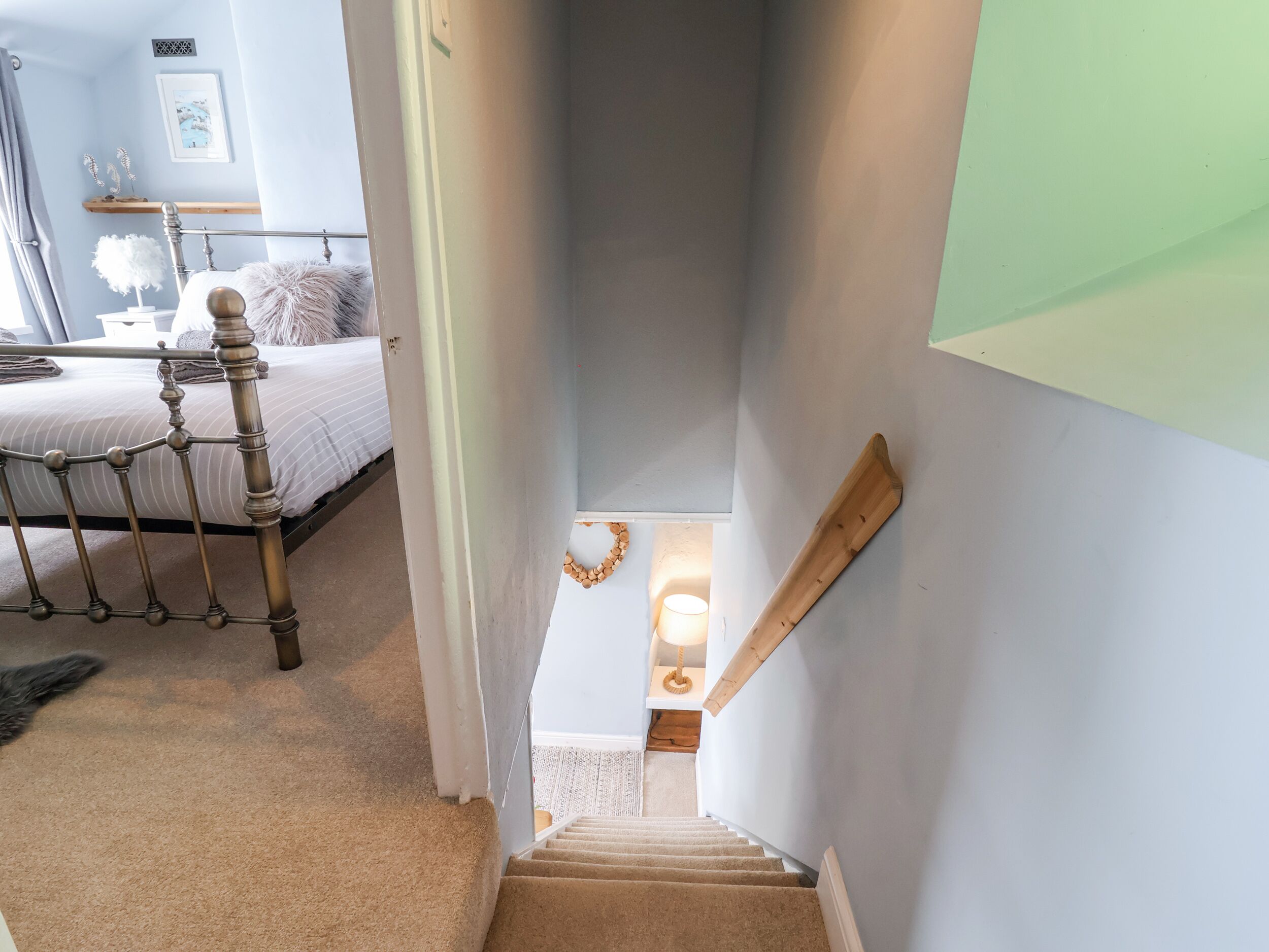 A staircase with a wooden handrail leading to a landing with a lamp and a small table.