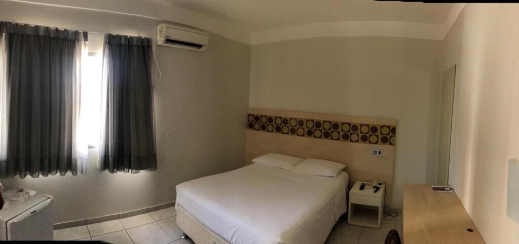A hotel room with a bed, bedside table, and a wall-mounted air conditioning unit.