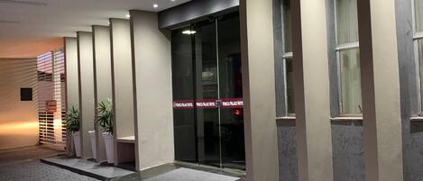 A hotel entrance with a modern design, featuring a glass door, potted plants, and a clear sign indicating the hotel name.