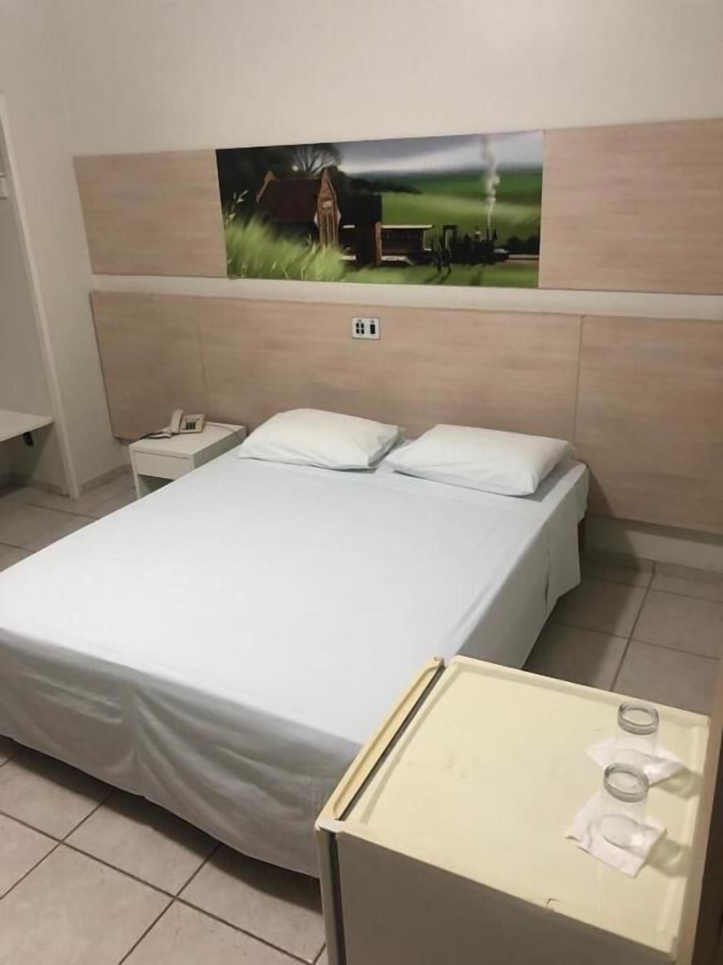 Une chambre à coucher avec un grand lit, une table de chevet avec un téléphone et une petite table avec une tasse et des mouchoirs.