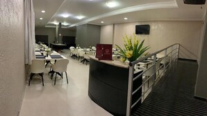 A hotel reception area with a curved desk, a red sign, and a staircase. - Veneza Palace Hotel (Cuiabá)
