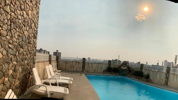 A rooftop pool with lounge chairs, a stone wall, and a view of the city skyline. - Veneza Palace Hotel (Cuiabá)