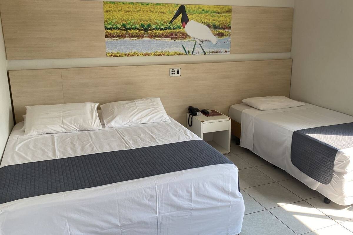 A hotel room with two single beds, a small bedside table with a phone, and a wall-mounted painting of a bird.