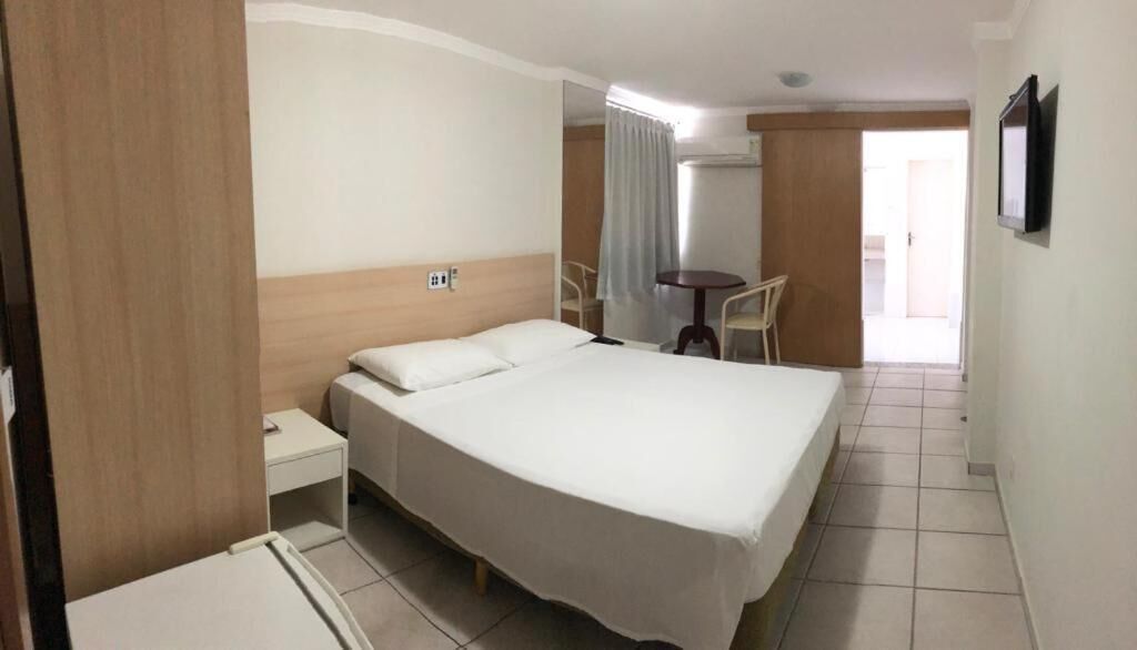 A hotel room with a large bed, a bedside table, a chair, a small table, and a TV.