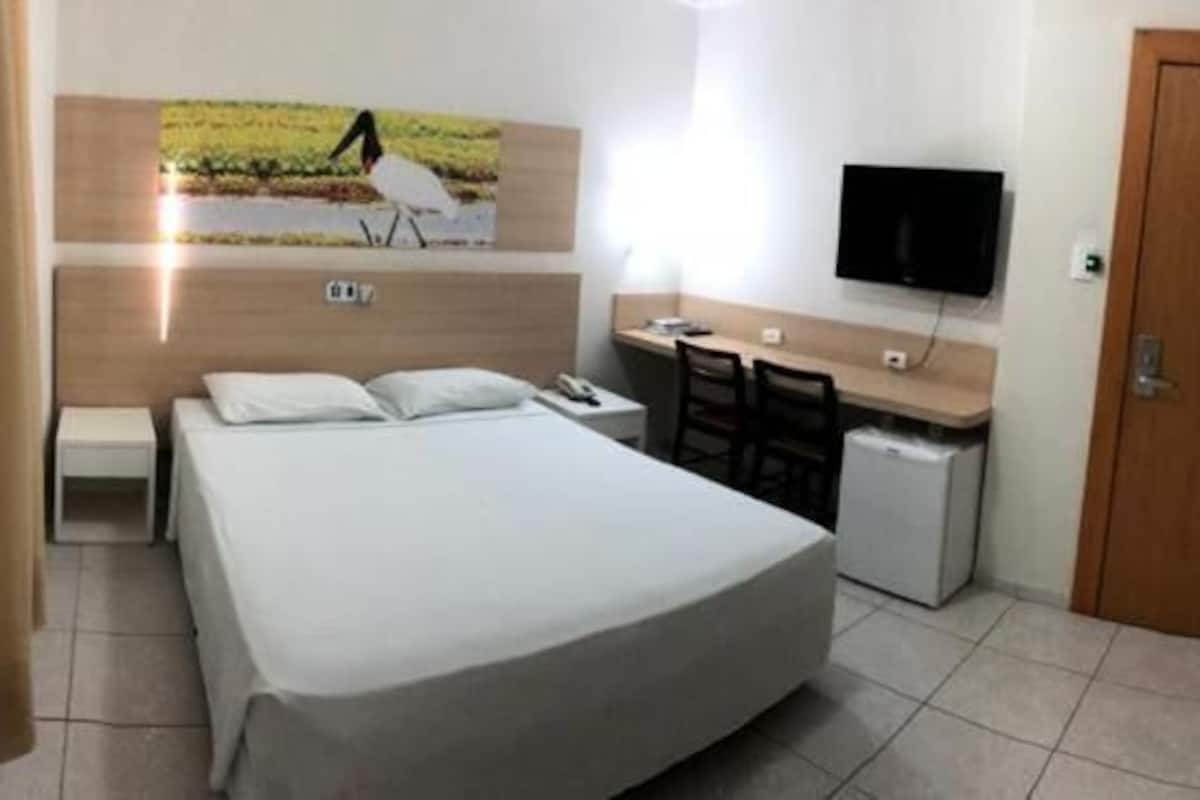 A hotel room with a bed, a desk, a chair, a television, and a door.