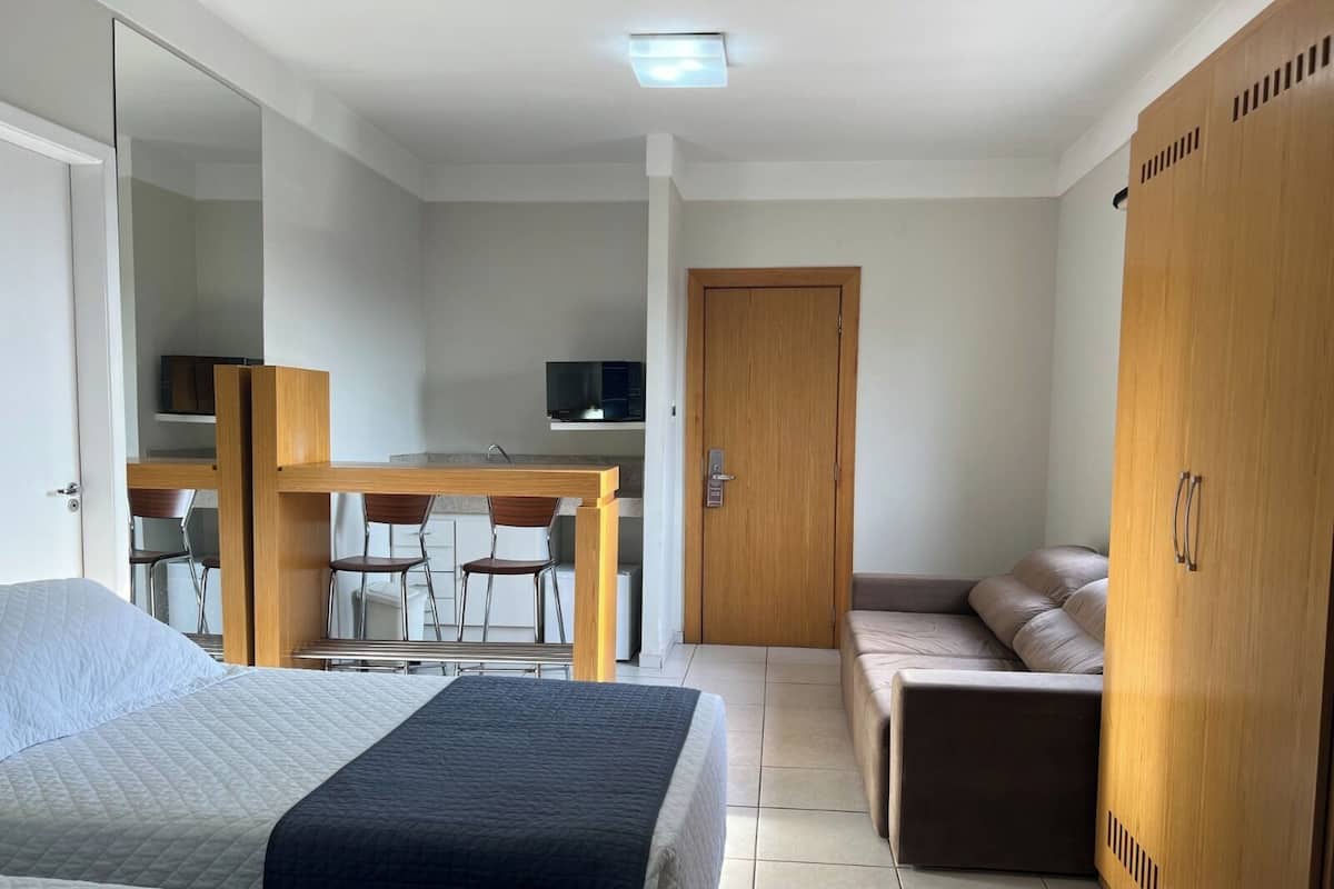 A hotel room with a bed, a sofa, a desk with chairs, and a wardrobe.