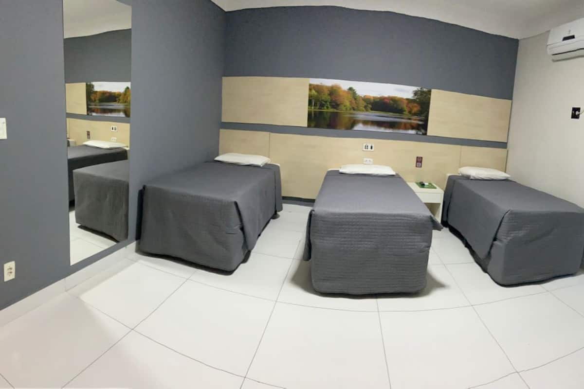 A room with three beds, a small table, and a large mirror.
